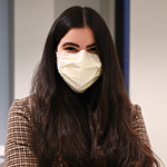 White female Drexel University student (Camryn Amen) with long brown hair wearing a checked jacket and white mask covering her nose and mouth.